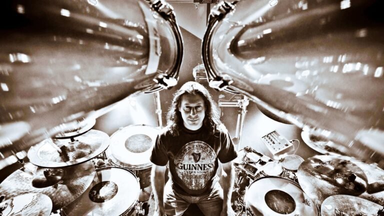 Mike Mangini performing live on drums behind a large kit, 2026